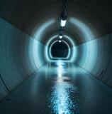 Tunnel interior with illuminated walls and wet floor, showcasing advanced construction materials and design.